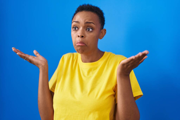 Afrikaans amerikaanse vrouw staan met twijfel uitdrukking over geïsoleerde blauwe achtergrond - Foto, afbeelding