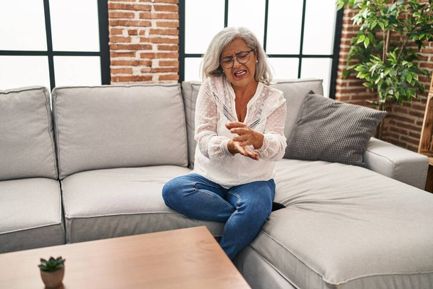 Frau mittleren Alters sitzt auf Sofa und leidet zu Hause unter Schmerzen am Handgelenk - Foto, Bild