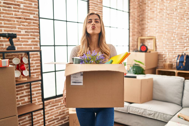 Young blonde woman moving to a new home holding cardboard box looking at the camera blowing a kiss being lovely and sexy. love expression.  - Photo, Image