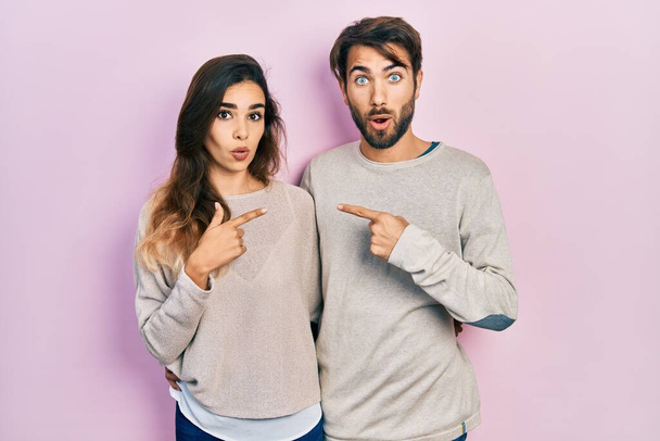 Junges hispanisches Paar in lässiger Kleidung überrascht mit dem Finger zur Seite zeigend, offener Mund erstaunter Ausdruck.  - Foto, Bild