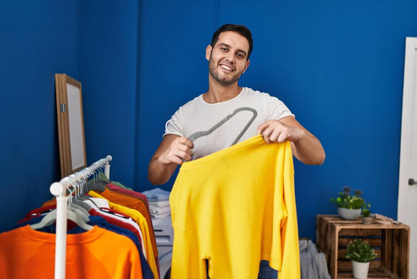 Giovane uomo ispanico mettere i vestiti su appendiabiti in lavanderia - Foto, immagini