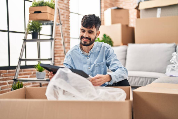 Молодий іспаномовний чоловік розпаковує картонну коробку в новому будинку
 - Фото, зображення