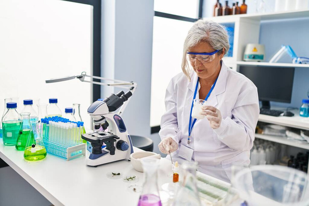 Middelbare leeftijd vrouw dragen wetenschapper uniform werken in laboratorium - Foto, afbeelding