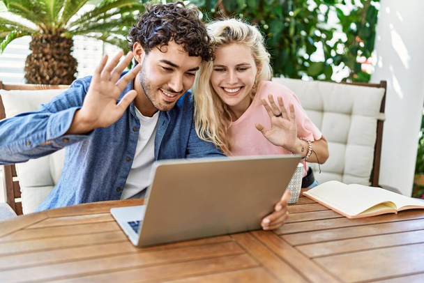 Junges Paar lächelt glücklich bei Videoanruf mit Laptop auf dem Tisch auf der Terrasse. - Foto, Bild