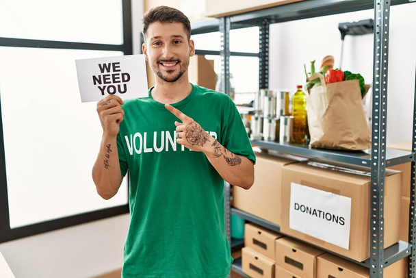 Νεαρός Ισπανός που φοράει εθελοντικό μπλουζάκι. Θέλουμε το πανό του να χαμογελάει χαρούμενος δείχνοντας με το χέρι και το δάχτυλο.  - Φωτογραφία, εικόνα