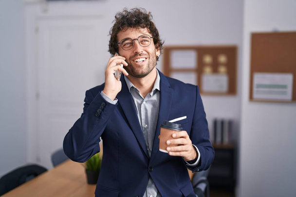 Young hispanic man business worker talking on smartphone drinking coffee at office - Zdjęcie, obraz