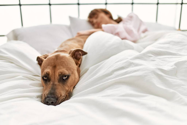 Молода біла жінка спить лежачи на ліжку з собакою в спальні
 - Фото, зображення
