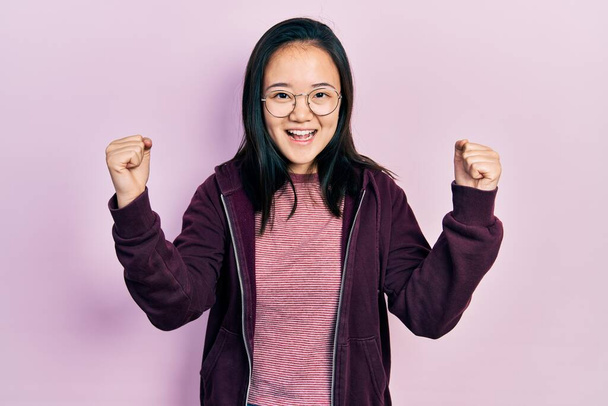 Young chinese girl wearing casual clothes and glasses screaming proud, celebrating victory and success very excited with raised arms  - Photo, Image
