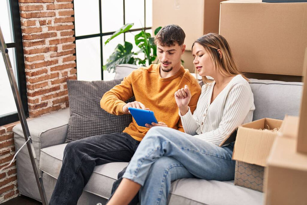 Young man and woman couple using touchpad sitting on sofa at new home - Foto, imagen