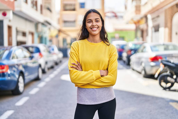 Fiatal afro-amerikai nő mosolyogva magabiztosan áll keresztbe tett kézzel az utcán - Fotó, kép