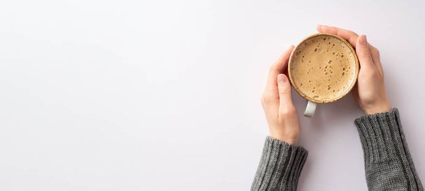 Autumn mood concept. Panoramic first person top view photo of girl's hands in grey pullover holding mug of frothy coffee on isolated white background with copyspace - Foto, Bild