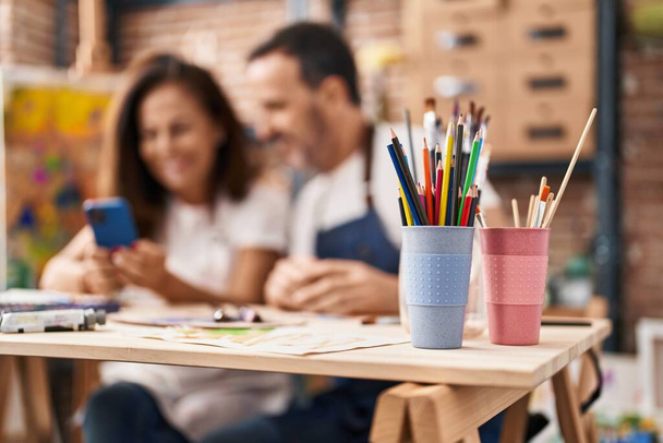 Мужчины и женщины средних лет рисуют на ноутбуке, используя смартфон в арт-студии - Фото, изображение