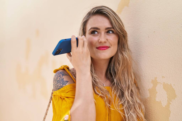 Jeune femme souriant confiant écoute message audio par le smartphone à la rue - Photo, image