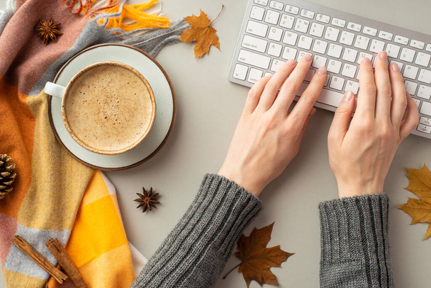 Autumn concept. First person top view photo of female hands in sweater typing on keyboard cup of coffee on saucer plaid yellow maple leaves anise pine cone cinnamon sticks on isolated grey background - Foto, Imagem