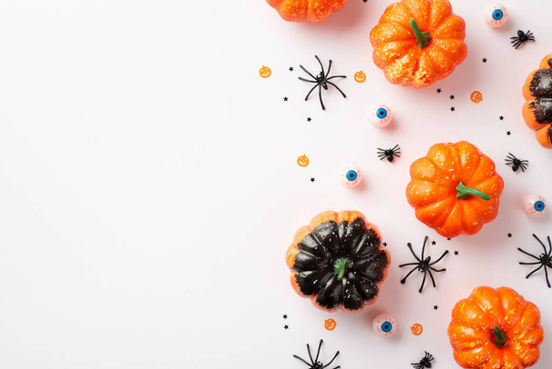 Концепция украшений для Хэллоуина. Вид сверху фото тыквы жуткие глаза пауки и конфетти на изолированном белом фоне с копирайтом - Фото, изображение