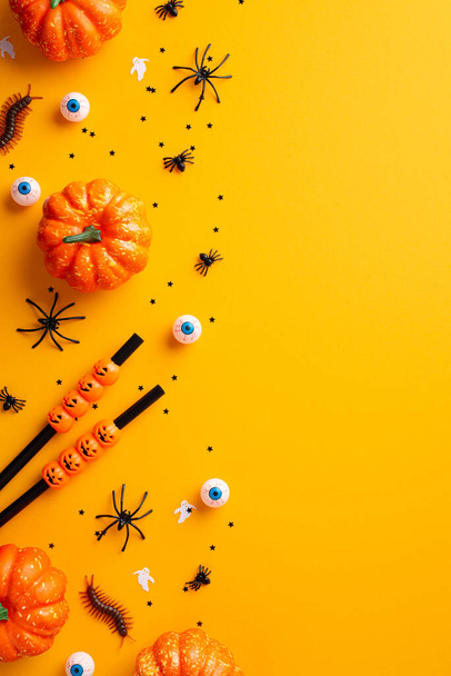 Halloween party concept. Top view vertical photo of cocktail straws pumpkins spiders centipedes creepy eyeballs and confetti on isolated orange background - Fotó, kép