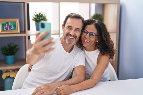 Чоловік і жінка роблять селфі за допомогою смартфона, сидячи на столі вдома
 - Фото, зображення