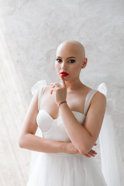 Bald beautiful bride in a luxurious wedding dress in red lipstick and a long veil is sick with cancer - Photo, image