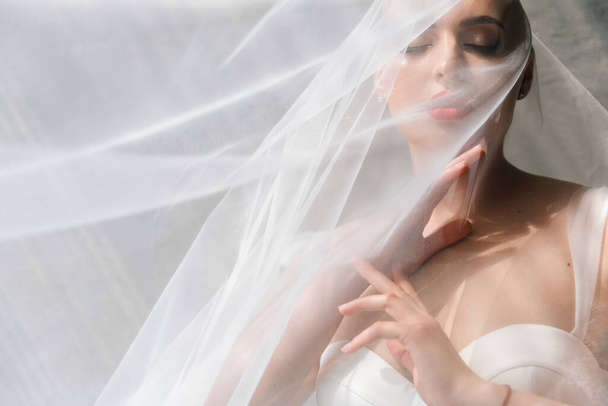 Bald beautiful bride in a luxurious wedding dress in red lipstick and a long veil is sick with cancer - Foto, afbeelding