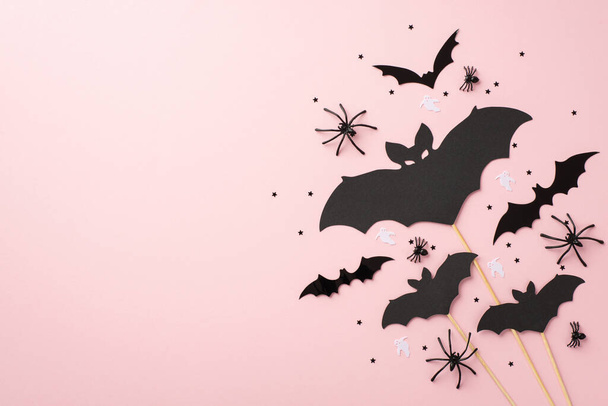 Halloween concept. Top view photo of bat silhouettes spiders ghost silhouettes and black confetti on isolated pastel pink background with empty space - Valokuva, kuva