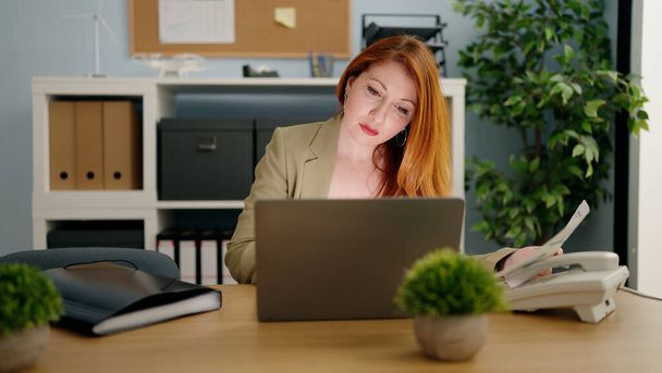 Fiatal vörös hajú nő üzleti dolgozó laptoppal dolgozik az irodában - Fotó, kép