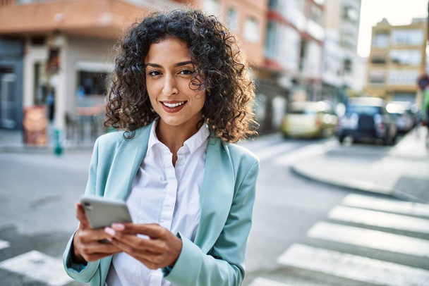Young hispanic business woman wearing professional look smiling confident at the city using smartphone - Photo, Image