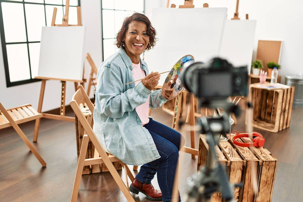 Блогер-латиноамериканец средних лет улыбается, имея видеозвонок в арт-студии. - Фото, изображение