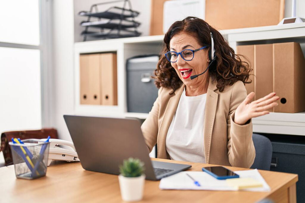 Middle age woman wearing call center agent headset celebrating achievement with happy smile and winner expression with raised hand  - Foto, immagini