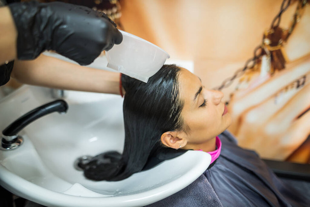 female client washes hair in salon, professional hairdresser washes head of female client with water and shampoo treatment, hairstyle beauty hair care, fashion service. - Foto, imagen