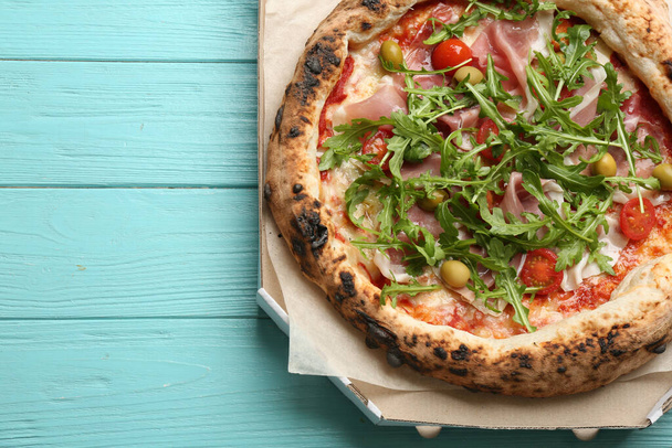 Tasty pizza with meat and arugula in cardboard box on light blue wooden table, above view. Space for text - Fotografie, Obrázek