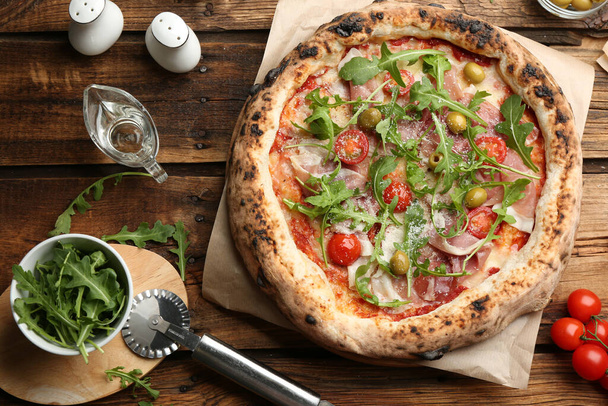 Tasty pizza with meat and arugula on wooden table, flat lay - Fotografie, Obrázek