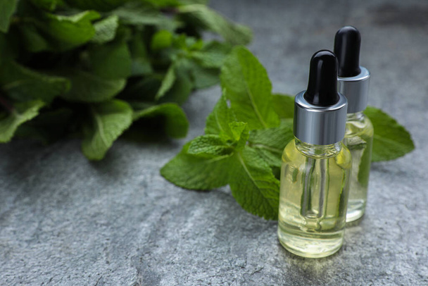 Bottles of essential oil and mint on grey table, closeup. Space for text - Zdjęcie, obraz