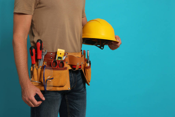 Professional builder with hard hat and tool belt on light blue background, closeup. Space for text - Fotoğraf, Görsel
