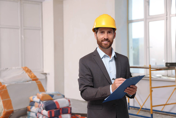 Professional engineer in hard hat with clipboard indoors - Фото, зображення