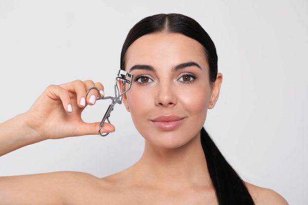 Beautiful young woman using eyelash curler on white background - 写真・画像