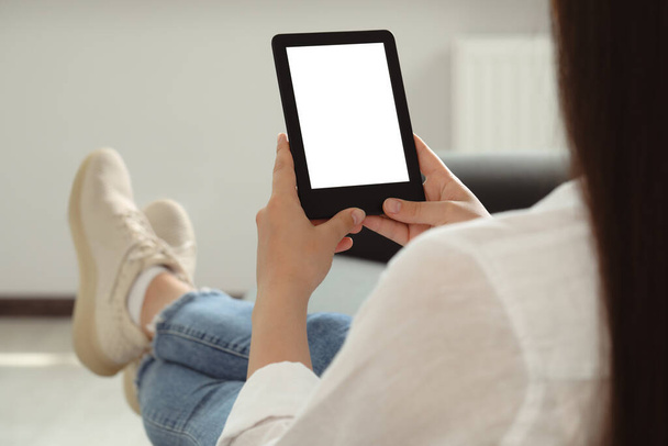 Young woman using e-book reader at home, closeup - Foto, afbeelding