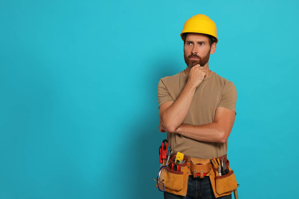 Professional builder in hard hat with tool belt on light blue background, space for text - Fotografie, Obrázek