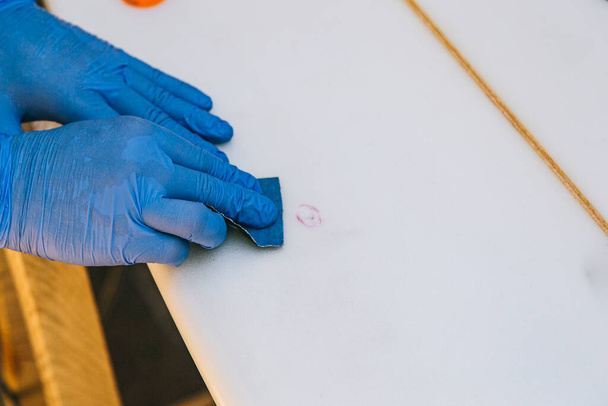 Surfer with protective gloves sanding a repair on the surfboard. - Photo, image