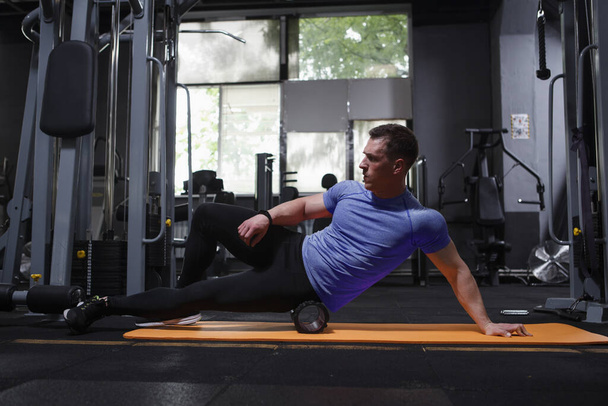 Professional athlete stretching muscles, using foam roller at the gym - Foto, imagen