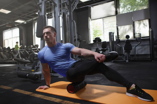 Professional bodybuilder using foam roller, stretching body muscles after workout at gym - Foto, Imagem
