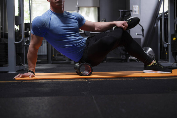 Cropped shot of a muscular sportsman using foam roller massager at the gym after sports workout - Фото, изображение