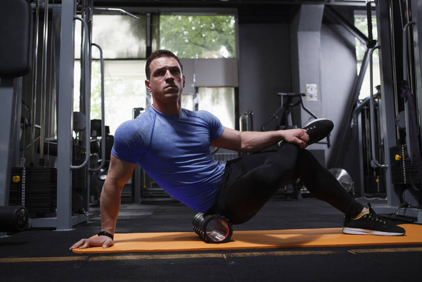 Male athlete relaxing muscles after working out, using foam roller at gym - Foto, immagini