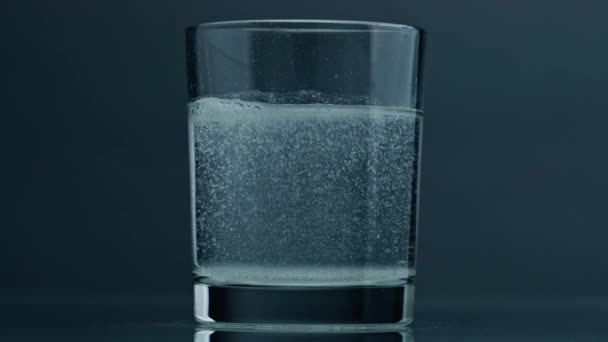 Air bubbles rising glass surface closeup. Acid fluid in transparent cup at dark background. Dissolved tablet painkiller bubbling in pure mineral water. Quenching thirst refreshing beverage concept. - Video