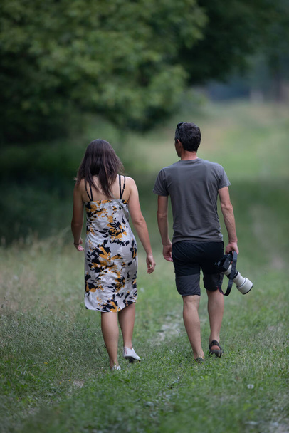Mature couple waking in forest in summer time while man carrying professional camera - Fotografie, Obrázek