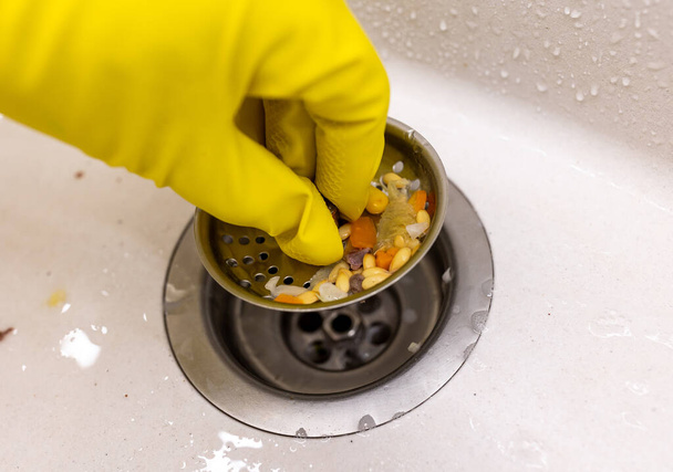 Close up of hand with protective glove holding sink disposal with food waste - Valokuva, kuva