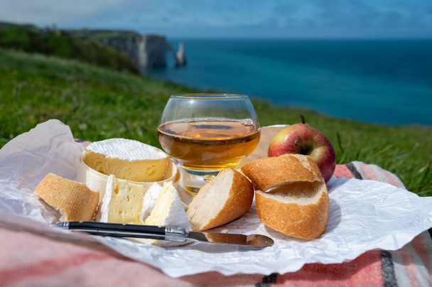 Almoço em campos de grama verde em falésias de giz de Etretat, camembert de queijo francês, baguete assada fresca e bebida de cidra de maçã com oceano Atlântico azul no fundo, Normandia, França - Foto, Imagem