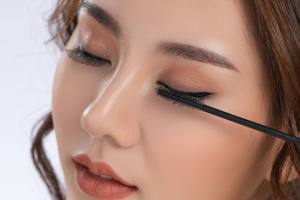 Closeup gorgeous young woman putting black mascara on her long eyelashes with brush. Beauty cosmetic concept. Female model with perfect skin. - Fotoğraf, Görsel