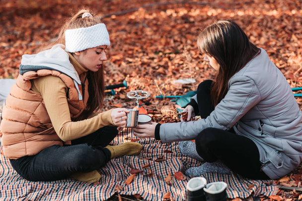 Two girls drinking hot tea from metal cups outdoor, camping - Фото, зображення