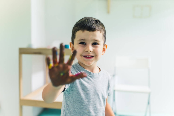 Χαριτωμένο λευκό αγόρι που δείχνει το ζωγραφισμένο του χέρι στο παιδικό δωμάτιο. Υψηλής ποιότητας φωτογραφία - Φωτογραφία, εικόνα