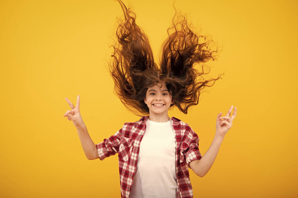 Úžasný teenager. Vzrušená dospívající dívka. Teenager portrét s bláznivými pohybovými vlasy. Mladé dospívající dítě s rozevlátými vlasy. Bruneta teen dívka chvějící se vlasy v pohybu, izolované na žlutém pozadí - Fotografie, Obrázek